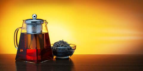 Warm teapot of tea with glass bowl with dry black tea, banner with copy space.