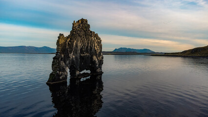 Hvitserkur basalt stack rock which looks like an elephant or dragon on the flowing water with view of mountains, sky and clouds during sunset