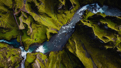 birdview of Fjadrargljufur canyon with a river meandering through the middle of the canyon with waves and water splash