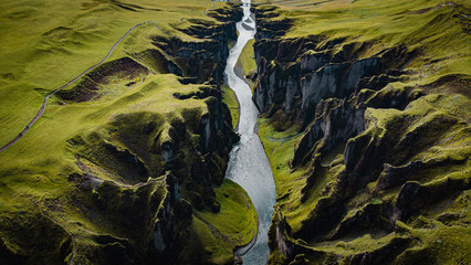 birdview of Fjadrargljufur canyon with a river meandering through the middle of the canyon and a trail on the side - obrazy, fototapety, plakaty
