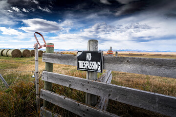 No Trespassing sign on a gate overlooking round hay bales and the Canadian Rocky Mountains on the Canadian prairies.
