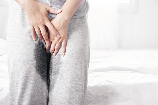 Stress Urinary incontinence concept with old woman wearing wet pants from urine standing next to her bed