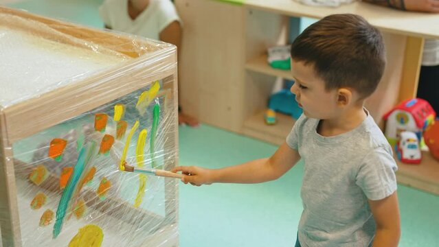 Little white boy in daycare nursery practicing painting on plastic wrap. Creative exercise for children. Horizontal indoor video. High quality 4k footage