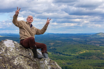 an elderly man Tourist sits on a rock on top of the Southern Urals ridge on a summer day