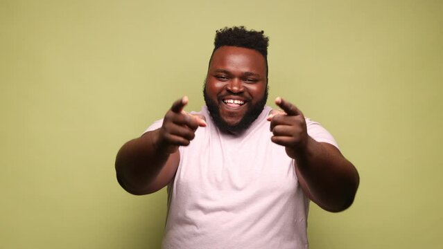 African-american man wearing pink t-shirt with cunning smile pointing fingers on you smiling at camera, victory in lottery, chance of success. Indoor studio shot isolated on light green background.