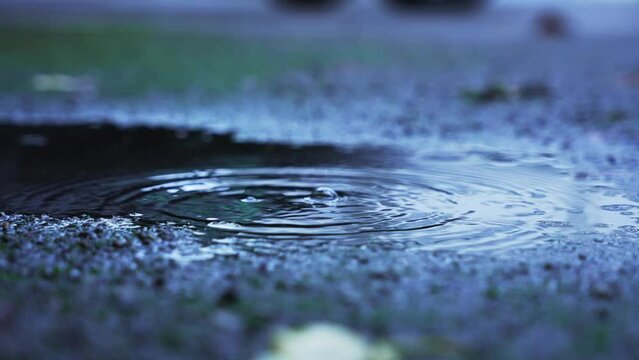 Three big water drops falling in a puddle on the concrete. Slowmotion camera pan.