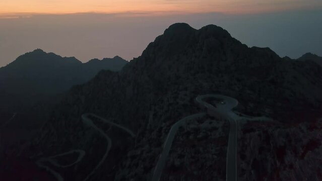 Aerial tilt up shot of famous serpentine road at Nus de Sa Corbata during dusk and golden hour