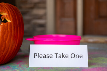 Bowl sitting on a doorway with a sign stating to please take one for Halloween trick or treaters. 