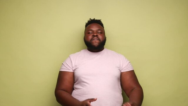 Dabbing movement. African-american man wearing pink t-shirt standing in dab dance pose, celebrating success, popular internet meme, dancing. Indoor studio shot isolated on light green background.