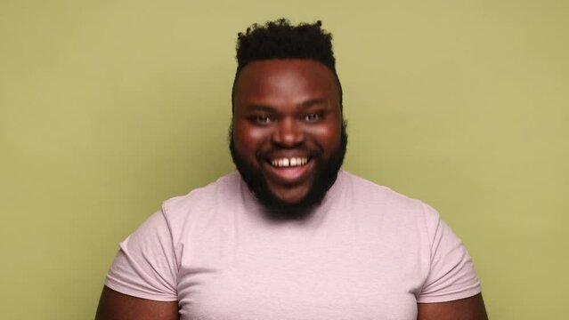 Extremely happy optimistic bearded African-american man wearing pink t-shirt standing looking at camera and nodding his head yes. Indoor studio shot isolated on light green background.