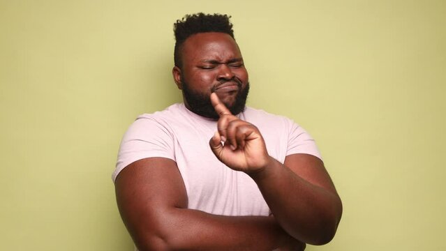 Happy funny young adult African-american man wearing pink t-shirt nodding no with head and finger, smiling with positive emotions. Indoor studio shot isolated on light green background.