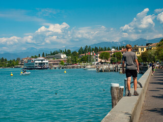 Sirmione harbor and ferry boat sail away. Boy walk on the wall
