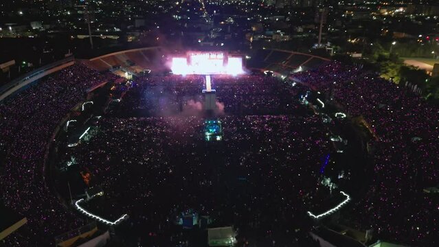 Aerial flyover of musical festival with celebrating crowd of people in open air stadium - Santo Domingo, Dominican Republic