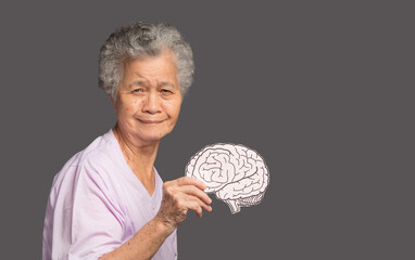 Portrait of a senior woman holding a brain symbol while standing on a gray background