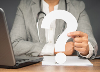 A doctor's holding a white question mark while sitting at the table in the hospital