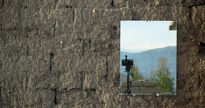Camera and mountain reflected in a mirror hanging on an adobe wall