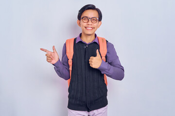 Look There. Smiling asian student man pointing his fingers away at copy space for your text or logo, isolated over gray studio background wall, banner, panorama. Smiling man showing thumbs up