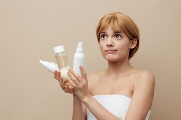 a funny, thoughtful woman stands on a beige background holding jars of care cosmetics in her hands and looks sadly away. Horizontal photo with empty space