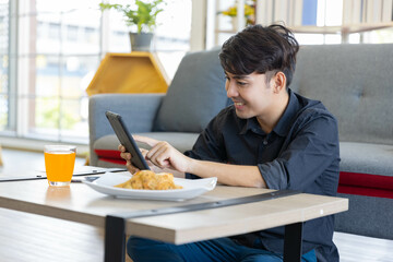 A handsome asian man is working from home using tablet in the living room in his home with snack and orange juice