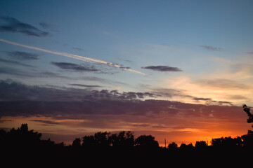 The morning glow illuminates the clouds on a beautiful colorful sky above the silhouettes of trees and a pillar at dawn