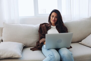 Woman freelancer on her day off sitting on the couch with a laptop at home and watching series and tv shows, smile