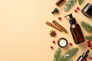 Winter skincare concept. Top view photo of amber pump bottle cream jar glass dropper bottles fir branches in frost mistletoe berries cinnamon sticks anise on isolated beige background with empty space