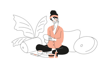 A young woman sits and looks in the mirror while applying cream to her face.