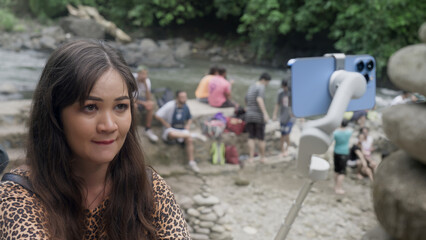 female video blogger with a tense face biting lips as she is filming a scene at river bank using...