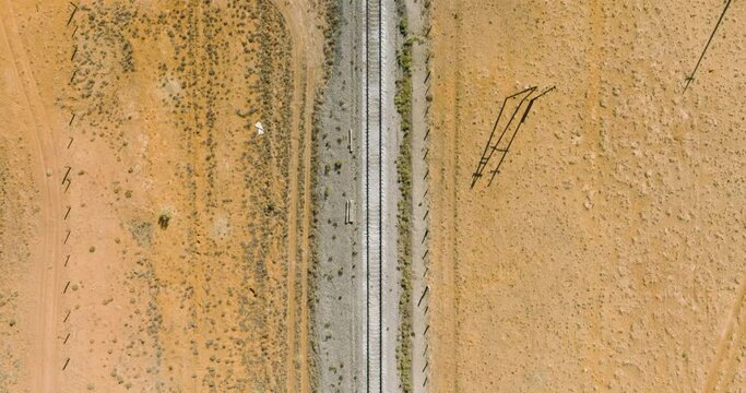Empty endless straight two-way railways through straight empty flat arid steppe. Aerial top down drone view.
