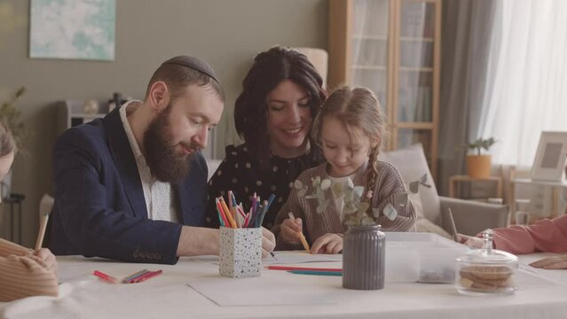 Modern cheerful Jewish family of five spending leisure time together at home drawing and chatting around table