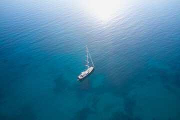 A large expensive high-speed sailing yacht is anchored on blue transparent water in the rays of the...