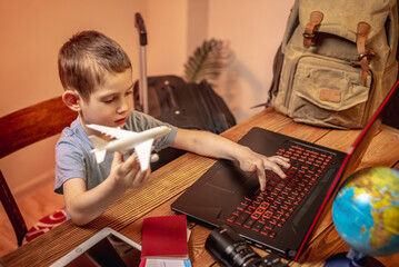 A child boy buys airline tickets for a laptop online at home. Traveling is easy, even a child can handle it