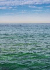 Fototapeta na wymiar The surface of the sea under a cloudy blue sky. Blue-green wave surface of the sea going to the horizon.