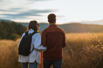 A girl is holding a boy's arm during their hike through a big golden yellow meadow on a sunset,...
