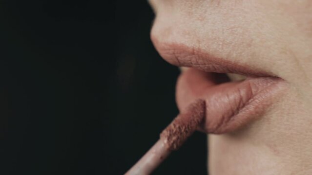 A woman does her own face makeup, applies lipstick and lip gloss. Close-up. The concept of beauty and fashion