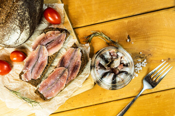 A set of pickled anchovies, in a glass jar. Fresh tomatoes and anchovy fillets on a wooden table. A jar of pickled anchovies.  Black bread and anchovies. Selective focus.