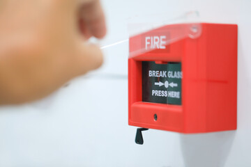 The hand of human is pressing fire alarm on the wall.