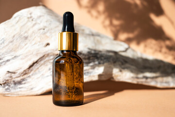 Glass bottle with an amber-colored pipette with facial serum on a natural dry wood background