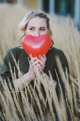 thoughtful young woman hoping or searching for self love and holding a red heart air balloon...