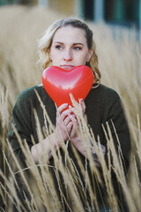 thoughtful young woman hoping or searching for self love and holding a red heart air balloon...