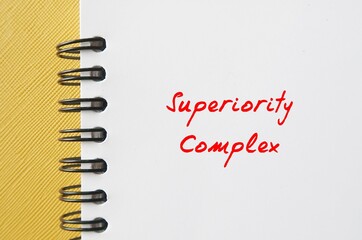 Notebook on yellow background with handwritten text SUPERIORITY COMPLEX, means belief that your...