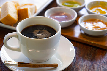 Hot Americano coffee in white cup on wooden desk with dessert and bread in the background