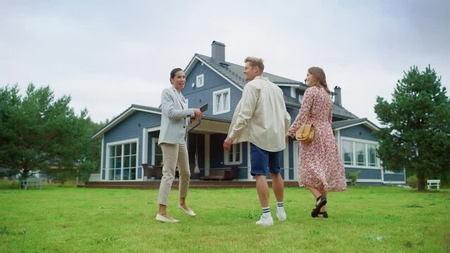Young Couple Visiting a Potential New Home Property with Professional Real Estate Agent. Realtor Showing a Beautiful Modern House with Traditional Suburban Design to a Young People. Slow Motion