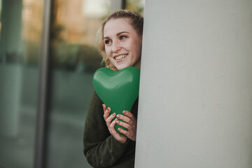 smiling young vegan girl full of joy holding a green heart air balloon in her hand for more...
