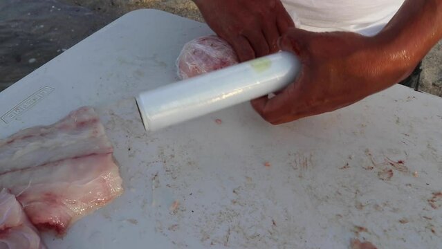 Rolling up a fish filet in saran wrap on a bloody table on the water