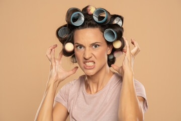 Beautiful angry woman with hair curlers posing on a beige background