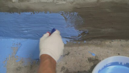 Waterproofing the floor with a brush.Waterproofing concrete mortar. The master puts waterproofing on a concrete floor with a brush. Bathroom floor waterproofing.