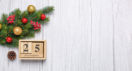 christmas tree branch with toys and gifts and wooden calendar december 25 on wooden background