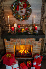 Many gift boxes near the Christmas fireplace in a festive interior of a Log Cabins with wooden walls. Mantelpiece with candles, Christmas wreath with bells