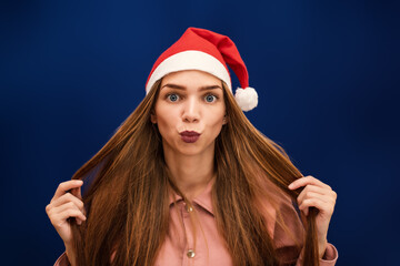 Woman in a Santa Claus hat on an isolated blue background sends a kiss